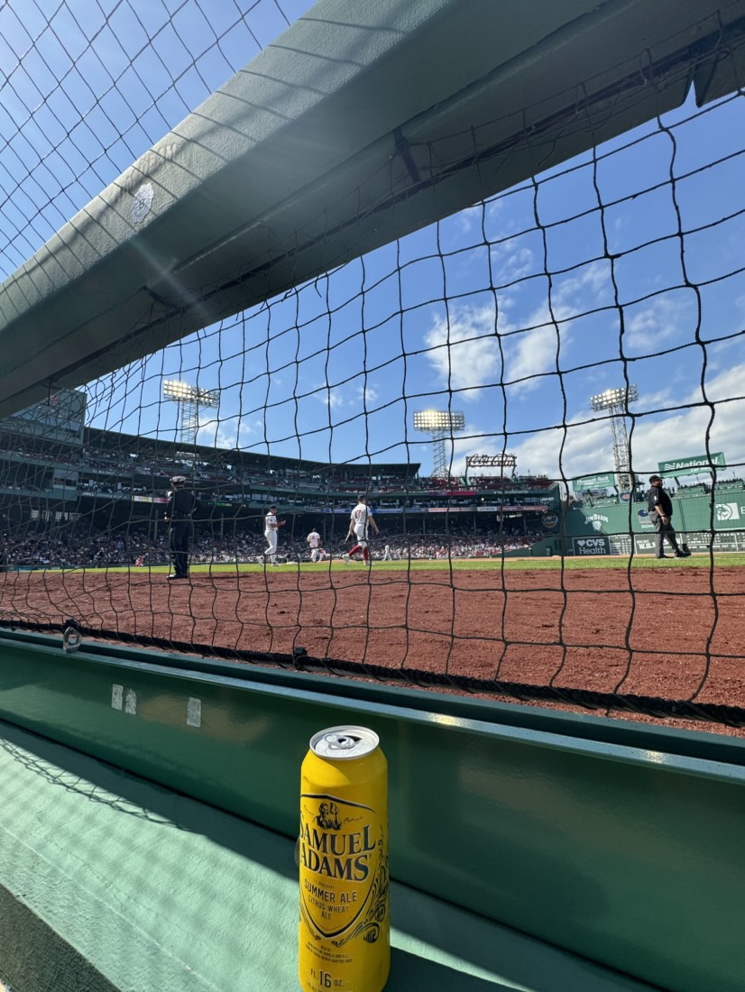 Field-level view through the netting at Fenway Park, with a Samuel Adams Summer Ale on the ledge